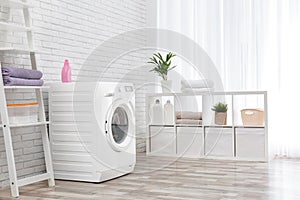 Modern washing machine near wall in laundry room interior