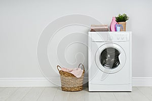 Modern washing machine with stack of towels, detergents and laundry basket near wall. Space for text