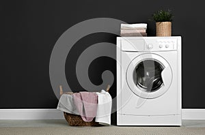 Modern washing machine with stack of towels, houseplant and laundry basket near wall. Space for text