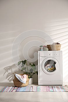 Modern washing machine and wicker basket with laundry near wall. Interior design