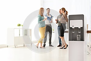 Modern water cooler with glass and blurred office employees on background