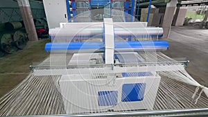 Modern weaving machine works with white strings at a textile plant. Textile factory equipment in work.