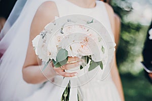 Modern wedding bouquet in bride hands. Gorgeous bride in white gown holding stylish bouquet of white and pink peonies and roses