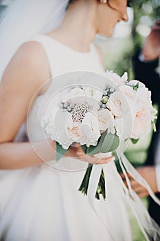 Modern wedding bouquet in bride hands. Gorgeous bride in white gown holding stylish bouquet of white and pink peonies and roses