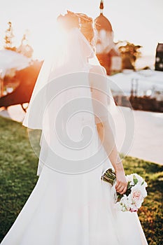 Modern wedding bouquet in bride hands in sunset. Gorgeous bride in white gown walking with stylish bouquet of white and pink