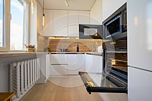 Modern white and beige wooden kitchen interior with oven opened