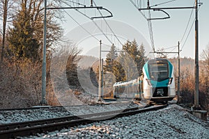 Modern white and blue passenger train in Slovenia, driving over a curve in the sunny winter time