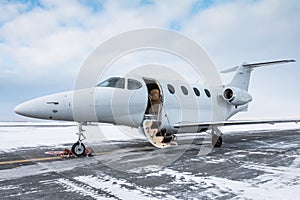 Modern white business jet with an opened gangway door at the winter airport apron