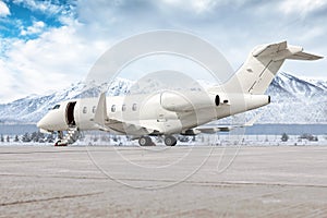 Modern white business jet with an opened gangway door at the winter airport apron on the background of high scenic snow capped