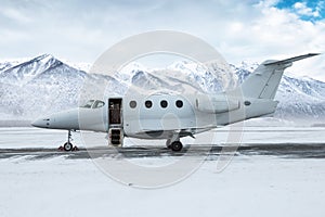 Modern white business jet with an opened gangway door at the winter airport apron on the background of high snow