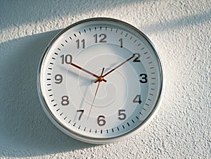 White clock showing time on textured wall in sunlight