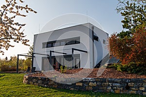 Modern, white, cube, elegant, minimalist style passive house with large panoramic windows, grey shutters in maintained garden in