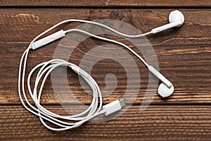 Modern white earphone, white in ear headphone on wooden table. White earphones over wooden board