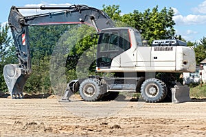 Modern white excavator standing on a ground. Digger with a bucket. Road work on an intercity highway