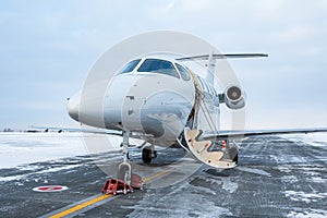 Modern white executive aircraft with an opened gangway door at the winter airport apron