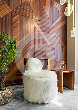 Modern white feather armless chair, small wooden modern table, planter with green bushes, decorated wood cladding wall