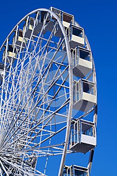 Modern white ferris wheel with closed glass booths against the blue sky. Close-up.