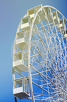 Modern white Ferris wheel with closed glass booths against a blue sky in the sun.