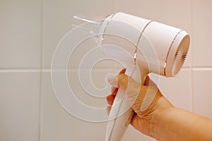 Modern white hair dryer for drying and styling hair in female hand, woman in bathroom dries hair after washing, hair care concept