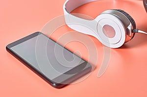 Modern white headphones with cable near smartphone or tablet on orange background