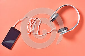 Modern white headphones with cable near smartphone or tablet on orange background
