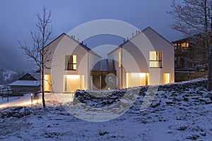 Modern white house with light windows surronded by mountain, snow and trees. Chirstmas mood