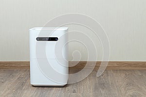 A modern white humidifier stands on the floor against the wall