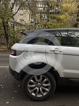 Modern white luxury SUV parked on urban street near trees