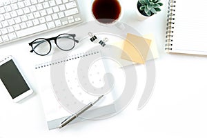 Modern white office desk table with computer, calendar, notebook, tree, glasses and cup of coffee. Top view with copy space