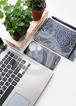 Modern white office desk table with laptop computer, smartphone with black screen and plants. Top view with copy space, flat lay