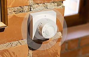 Modern white room and floor heating controller on a brick wall, close-up. Adjustment of the comfortable temperature in the room