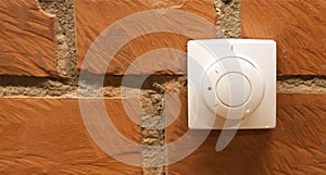 Modern white room and floor heating controller on a brick wall, close-up. Adjustment of the comfortable temperature in the room.