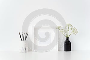 Modern white square frame mockup with a Aegopodium in black vase and black pencils on white background.