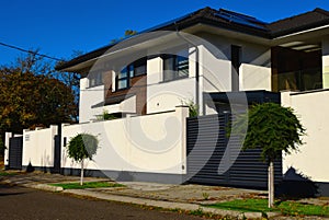 Modern white stucco finished house with solid white fence and small evergreen trees