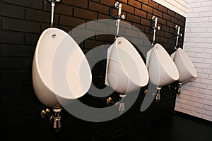 Modern white urinals in a men\'s public restroom on a decorative brick wall