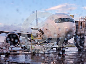Modern wide fuselage jet airliner parked in the airport seen through the glass with raindrops standing on wet tarmac