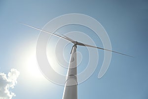 Modern wind turbine against blue sky, low angle view. Energy efficiency