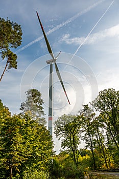 Modern wind turbine during daylight view from low angle with forest in front