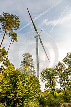 Modern wind turbine during daylight view from low angle with forest in front