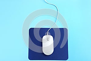 Modern wired mouse and pad on blue background, top view