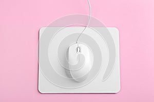 Modern wired mouse and white pad on background, top view