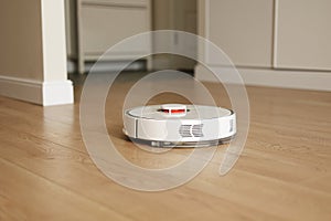 Modern wireless autonomous robotic vacuum cleaner cleans living room. Smart self-propelled white cleaning robot washes