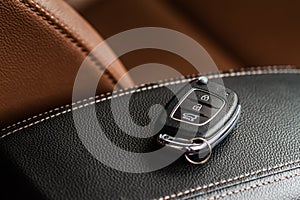Modern wireless car key on darl leather in car interior.