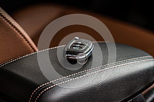 Modern wireless car key on darl leather in car interior.