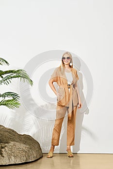 Modern woman in beige outfit posing by rock and plant