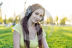 Modern woman with dreadlocks listening to music with her headphones in autumn Sunny Park. Concept of good mood