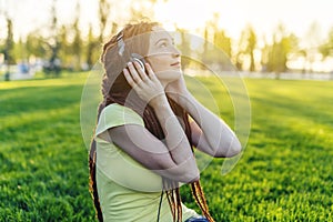 Modern woman with dreadlocks listening to music with her headphones in autumn Sunny Park. Concept of good mood