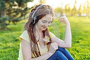Modern woman with dreadlocks listening to music with her headphones in autumn Sunny Park. Concept of Melomania