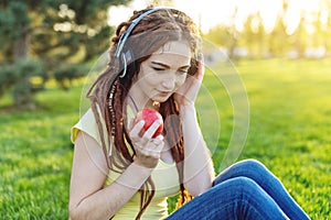 Modern woman with dreadlocks listening to music with her headphones in autumn Sunny Park. Concept of Melomania