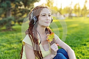 Modern woman with dreadlocks listening to music with her headphones in autumn Sunny Park. Melomania and good mood